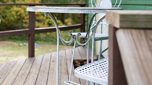 Eine Holzterrasse mit einem Metalltisch und -stühlen, einer amerikanischen Flagge und einem grünen Haus mit Fenster und Tür.
