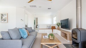 Ein modernes Wohnzimmer mit einem grauen Sofa, einem Holztisch, einem Fernseher und einem Kaminofen.