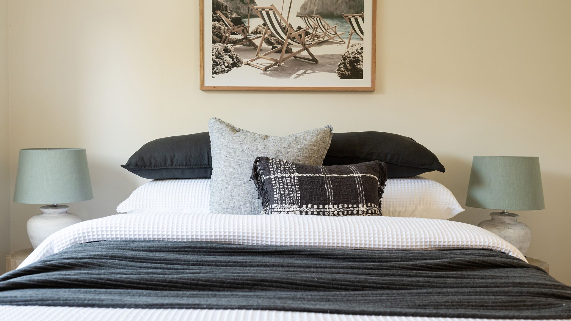 A neatly made bed with a striped blanket, two pillows, and a framed picture above it. There are two bedside lamps on either side of the bed.