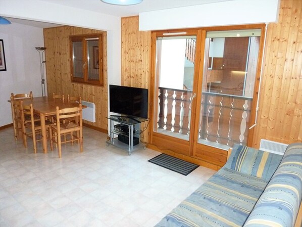 Uma sala de estar com piso de madeira, uma televisão sobre um móvel, uma mesa de jantar com cadeiras e um sofá.