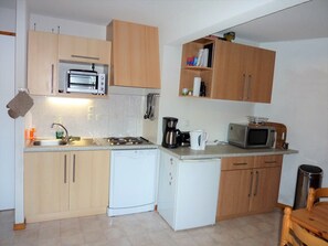 Uma cozinha compacta com armários de madeira, micro-ondas, fogão, pia e uma geladeira pequena.