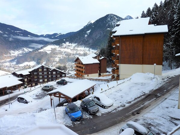 A snow-covered mountain town with wooden buildings, a parking area, and a road.