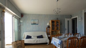 A room with a bed, a dining table set for four, a wooden cabinet, and a ship painting on the wall. - 3-bedroom apartment with large balcony and garage near the casino (Saint-Jean-de-Monts)