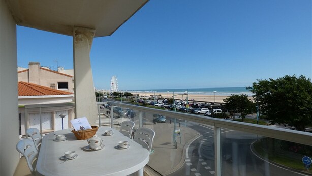 A balcony with a table set for tea, overlooking a beach and a parking lot. - 3-bedroom apartment with large balcony and garage near the casino (Saint-Jean-de-Monts)