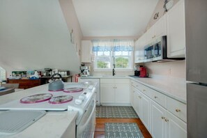 A kitchen with white cabinets, a stove, a microwave, and a window with curtains.
