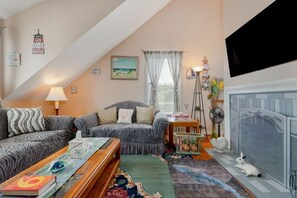 A cozy living room with a sofa set, a fireplace, and a television mounted on the wall.