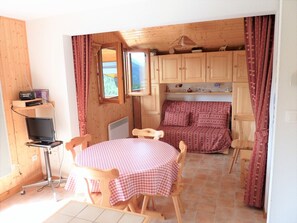 A cozy room with a round table, a bed with patterned bedding, wooden cabinets, and a window with curtains.