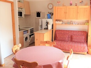 A compact kitchen with a washing machine, microwave, and wooden cabinets.