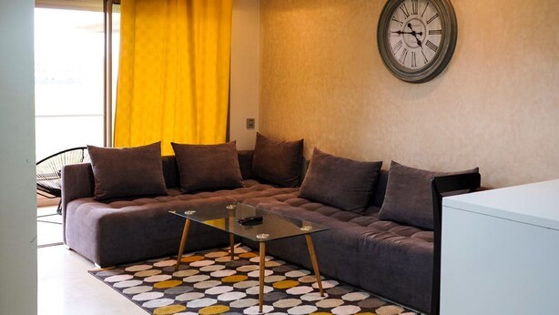 A modern living room with a sofa, a coffee table, a clock on the wall, and a window with yellow curtains. - PRESTIGIA GOLF CITY MARRAKECH (Marrakech)