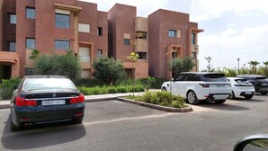 A parking lot with several cars, a building with a modern design, and some greenery. - PRESTIGIA GOLF CITY MARRAKECH (Marrakech)
