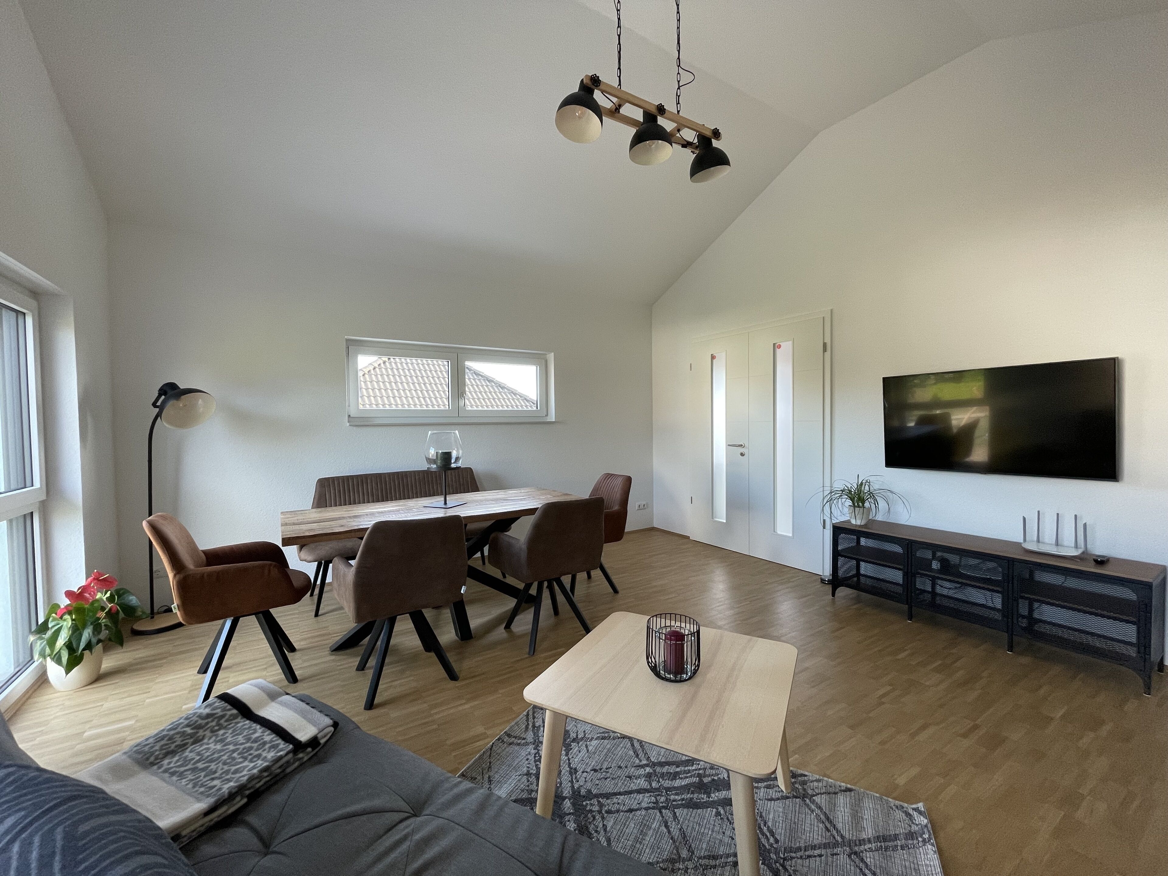 A spacious living area with a dining table, chairs, a sofa, a TV, and a small table with a candle.