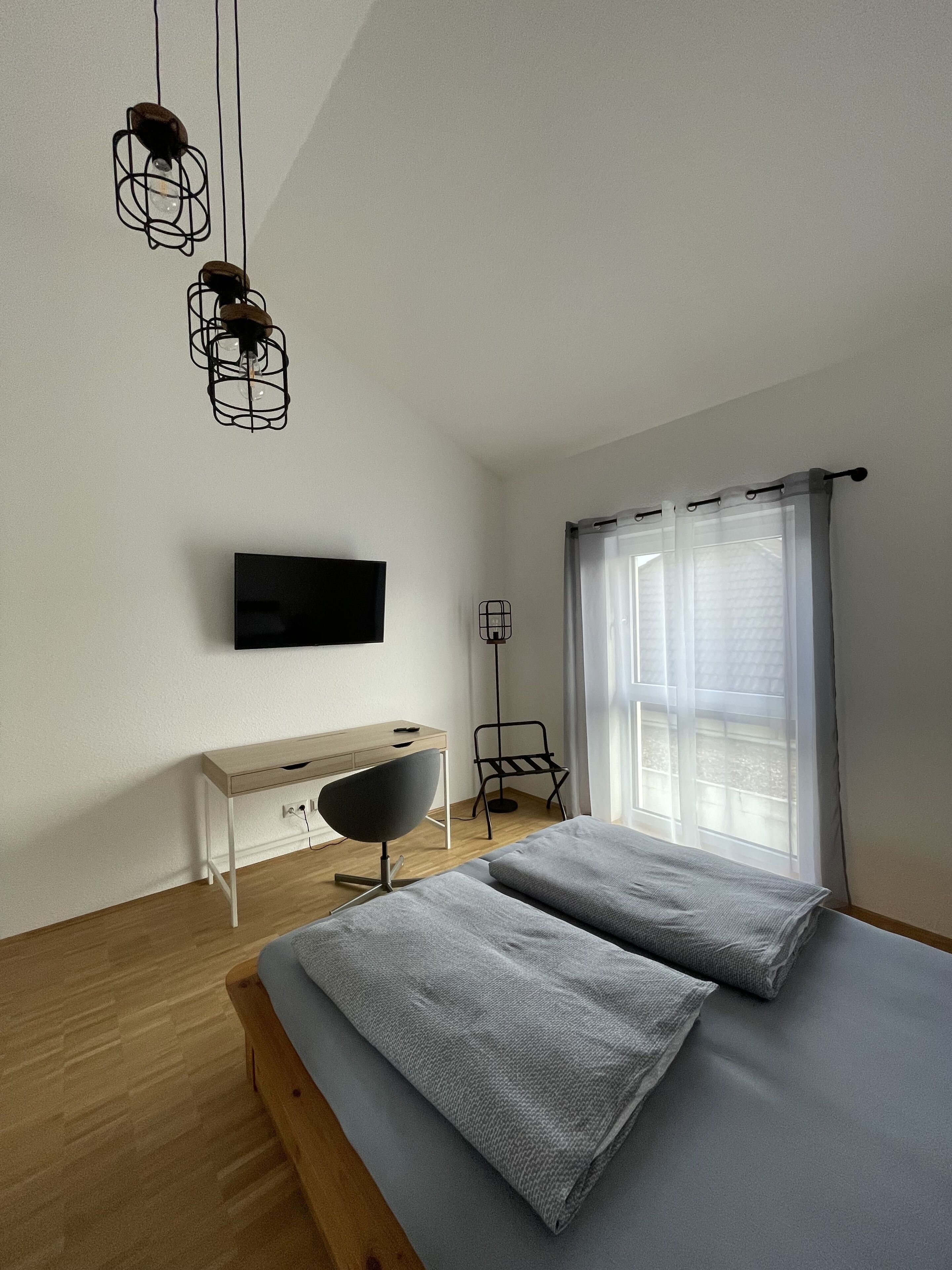 Un dormitorio moderno con cama, escritorio, silla, televisor y lámpara de pie.