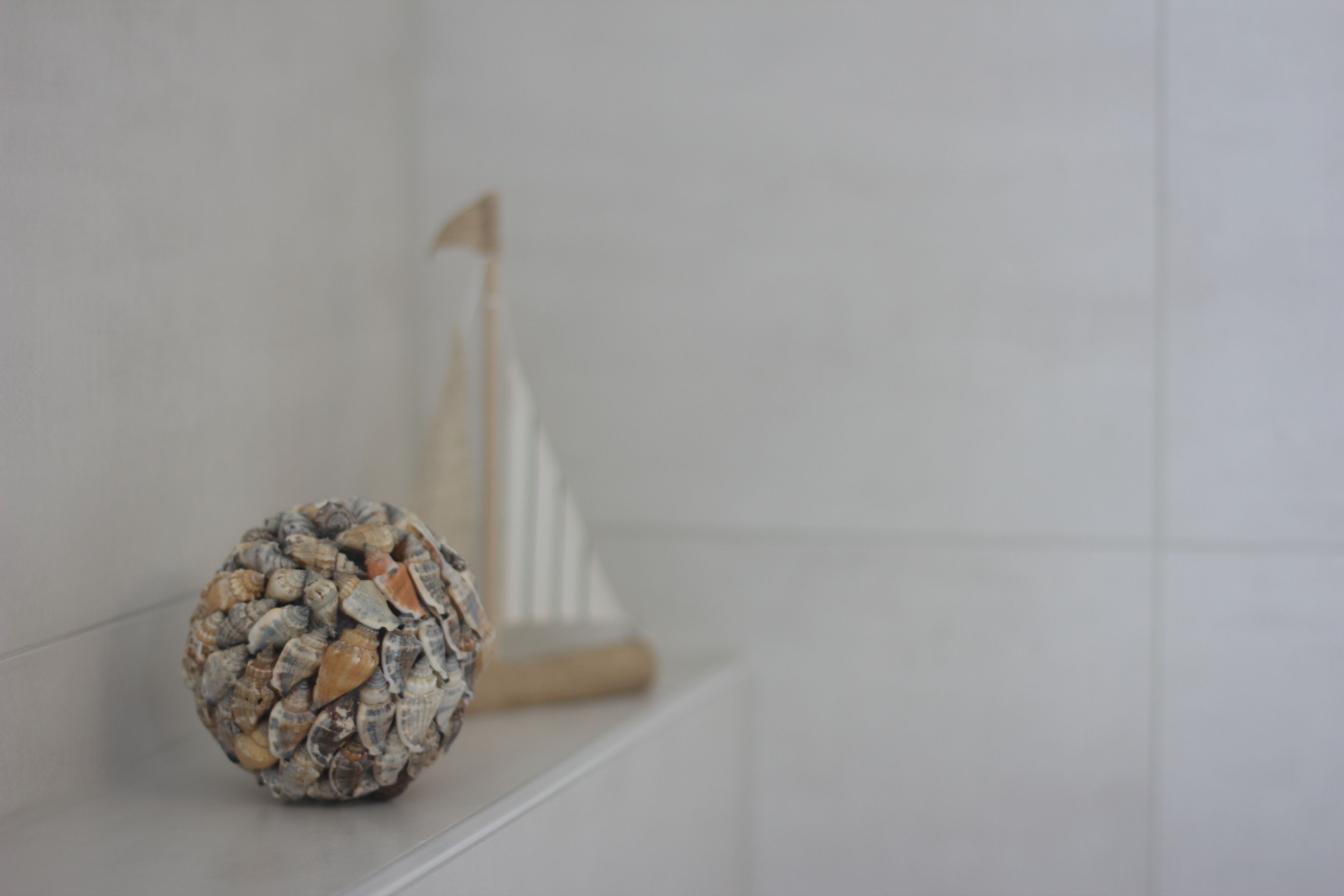 A decorative shell on a white shelf with a small wooden boat model in the background.