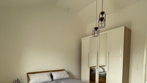 A bedroom with a wooden bed, grey bedding, a nightstand with a lamp, and a wardrobe. - Modern "industrial style" vacation apartment with terrace + nearby playground (Parthenstein)