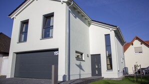 A modern two-story house with a garage, large windows, and a well-maintained lawn. - Modern "industrial style" vacation apartment with terrace + nearby playground (Parthenstein)