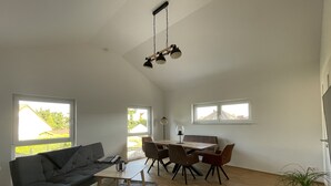 A spacious living room with a sofa, dining table, chairs, and a hanging light fixture. - Modern "industrial style" vacation apartment with terrace + nearby playground (Parthenstein)