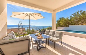 Terraço com mesa, cadeiras, uma cadeira suspensa e piscina.