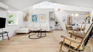 Een ruime loft met hoge plafonds, een eethoek met een moderne tafel en stoelen, een zithoek met een bank en salontafel, en kunstwerken aan de muur.