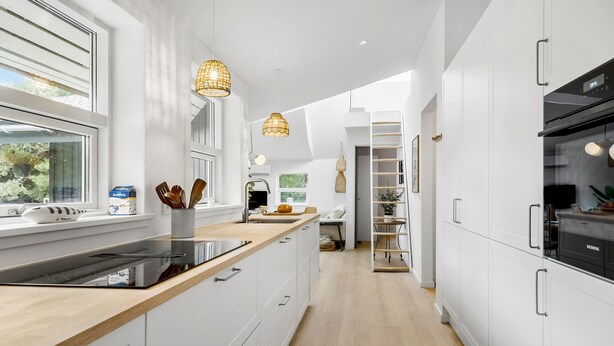 Een moderne keuken met witte kastjes, een houten aanrechtblad en een inbouwoven. Er zijn hangende吊り下げ式のペンダントライトと、 groene buitenpartij zichtbare raam.