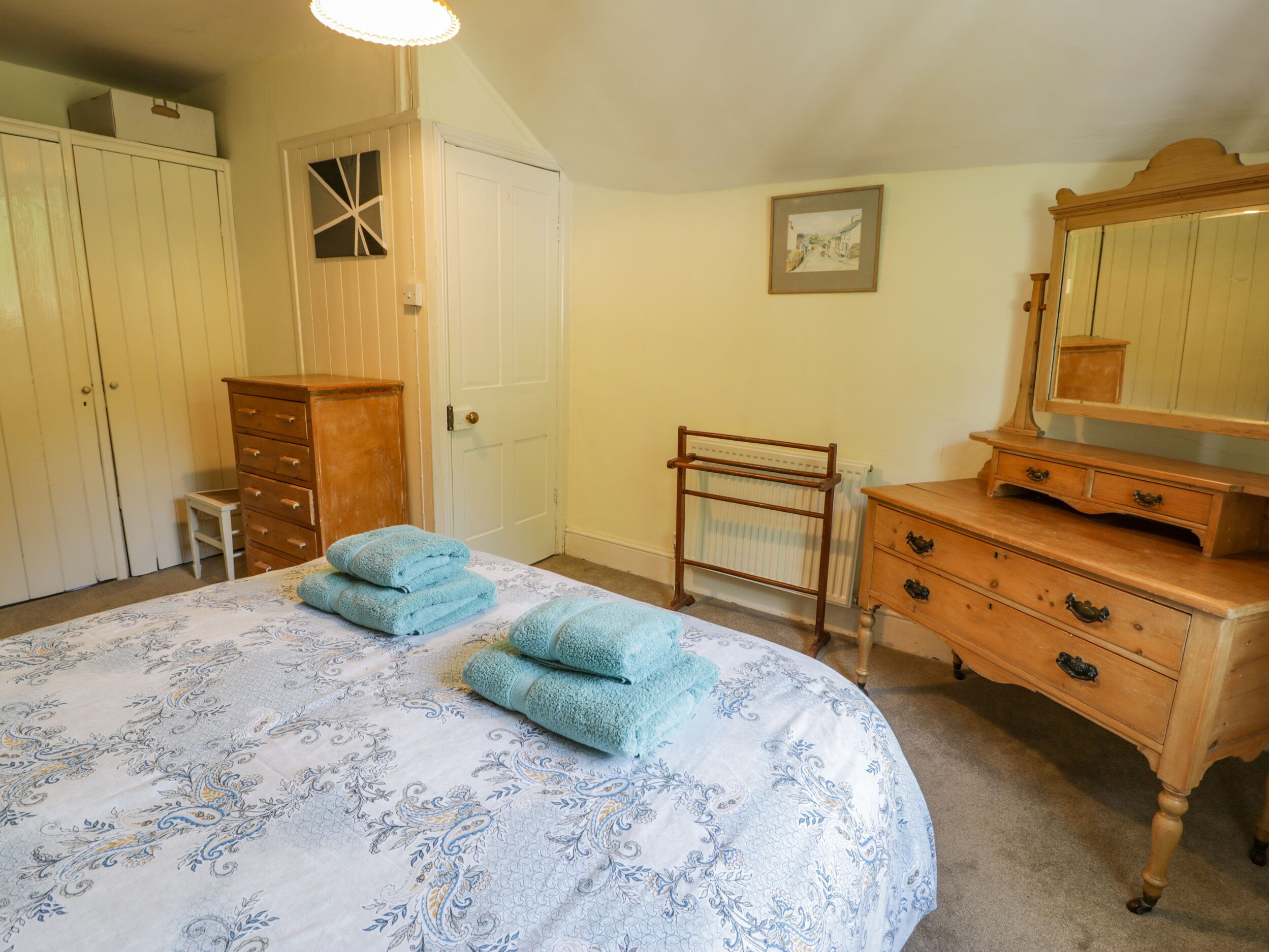 Un dormitorio con cama, cómoda, espejo y radiador.