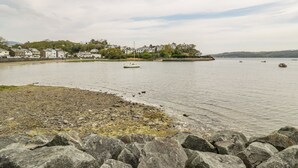 Un pueblo costero con un litoral rocoso, un pequeño velero y casas al fondo.