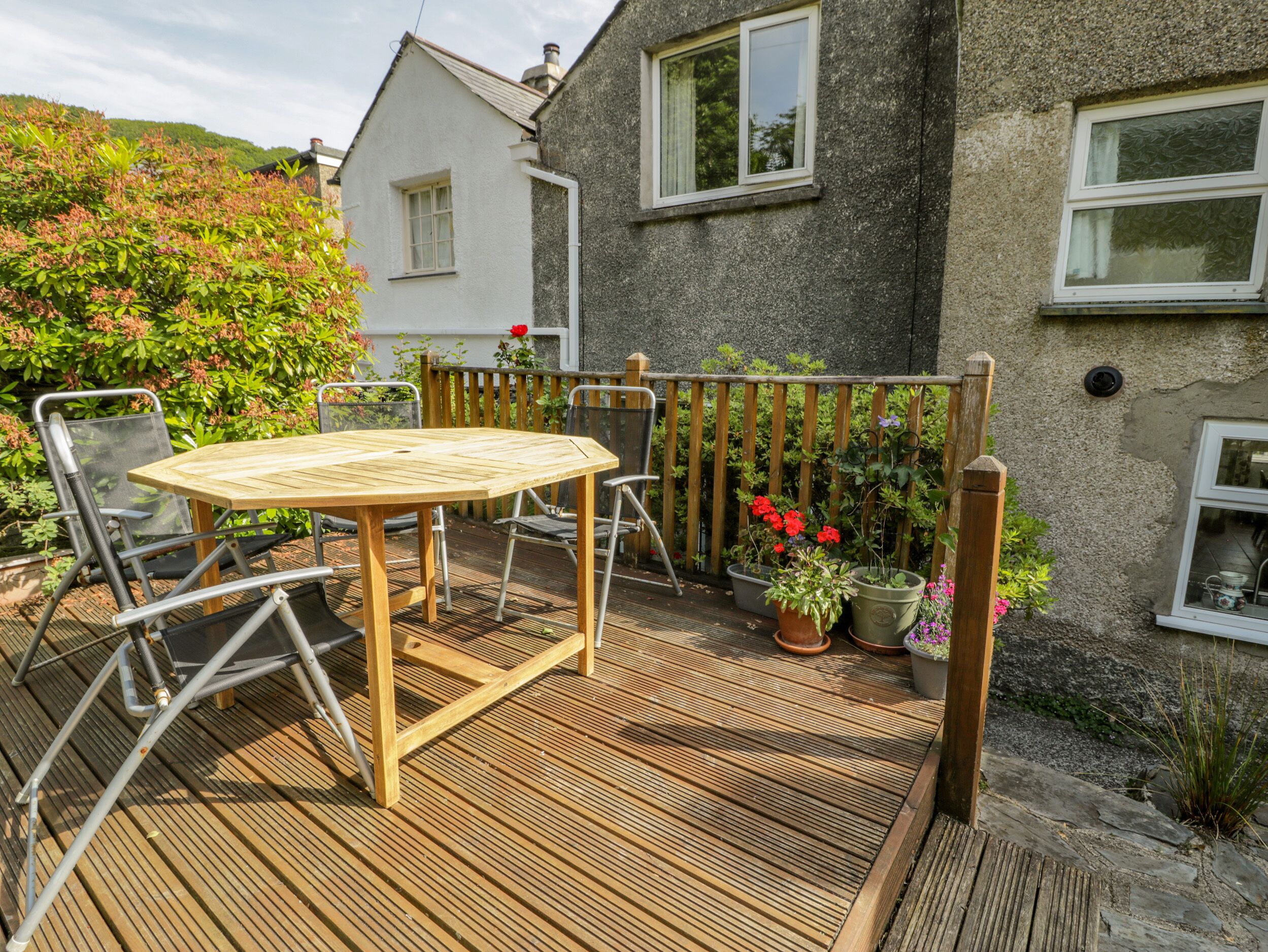 A wooden deck with a round table and chairs, surrounded by potted plants and a wooden fence.