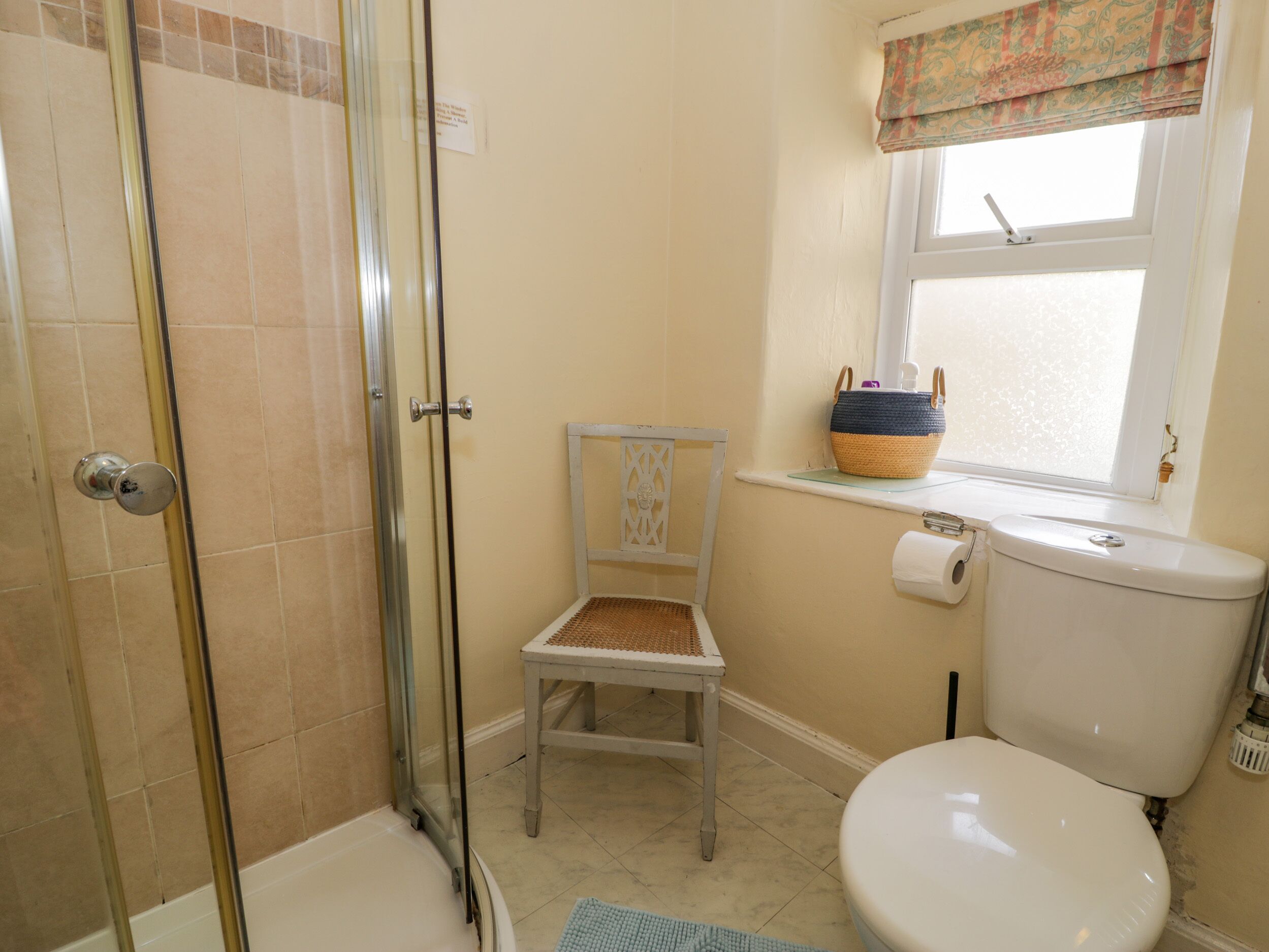 Un bagno con doccia, WC e una sedia vicino a una finestra.
