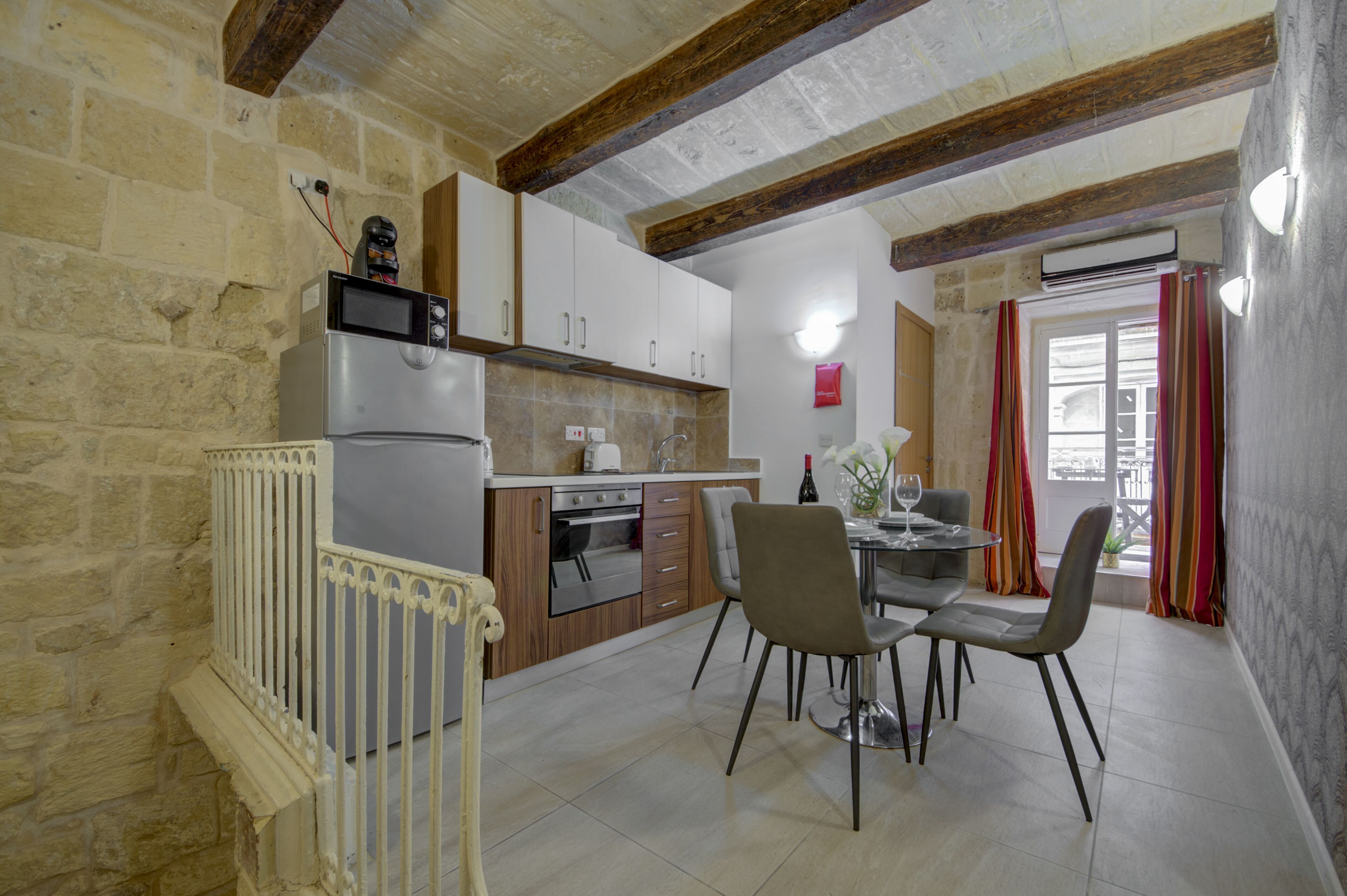 Une cuisine avec un coin repas, des murs en pierre, des poutres en bois et une fenêtre avec des rideaux.