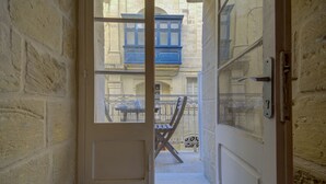 A narrow doorway leading to a balcony with a table and chairs, a window with blue shutters, and a door with a handle. - Tritoni harbour suites (Valletta)