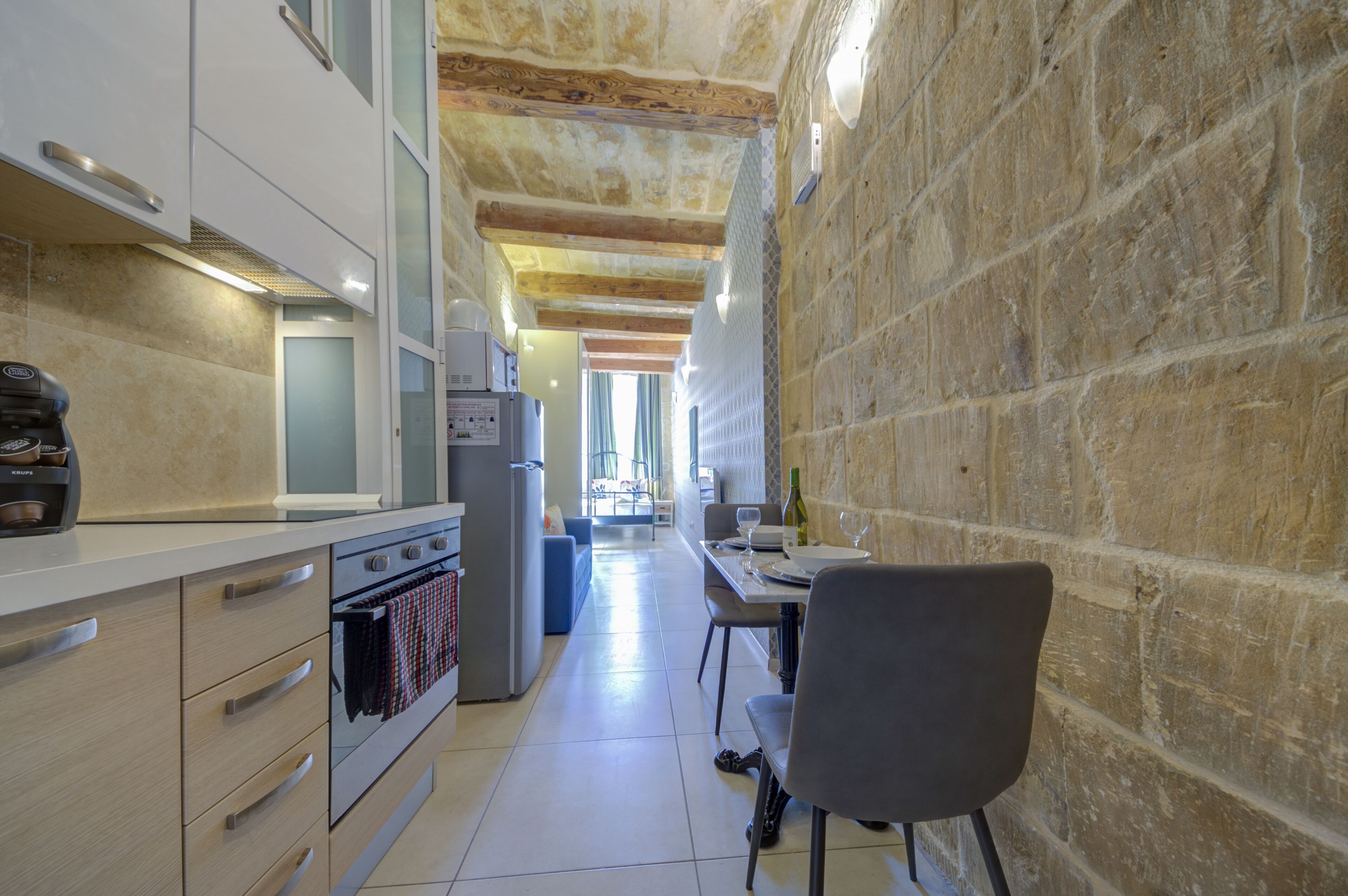 Cocina estrecha con paredes de piedra, comedor con mesa y sillas, y vista al salón.