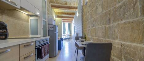 Cocina estrecha con paredes de piedra, comedor con mesa y sillas, y vista al salón.