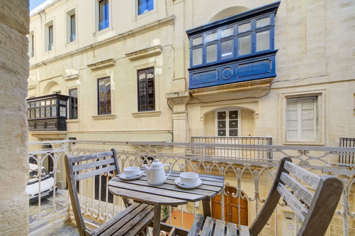 A balcony with a wooden table, two white cups, and a white teapot.