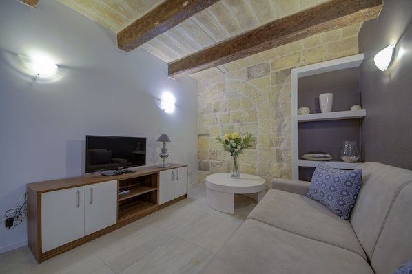 Una sala de estar moderna con televisor, sofá y una pequeña mesa redonda con un jarrón de flores.