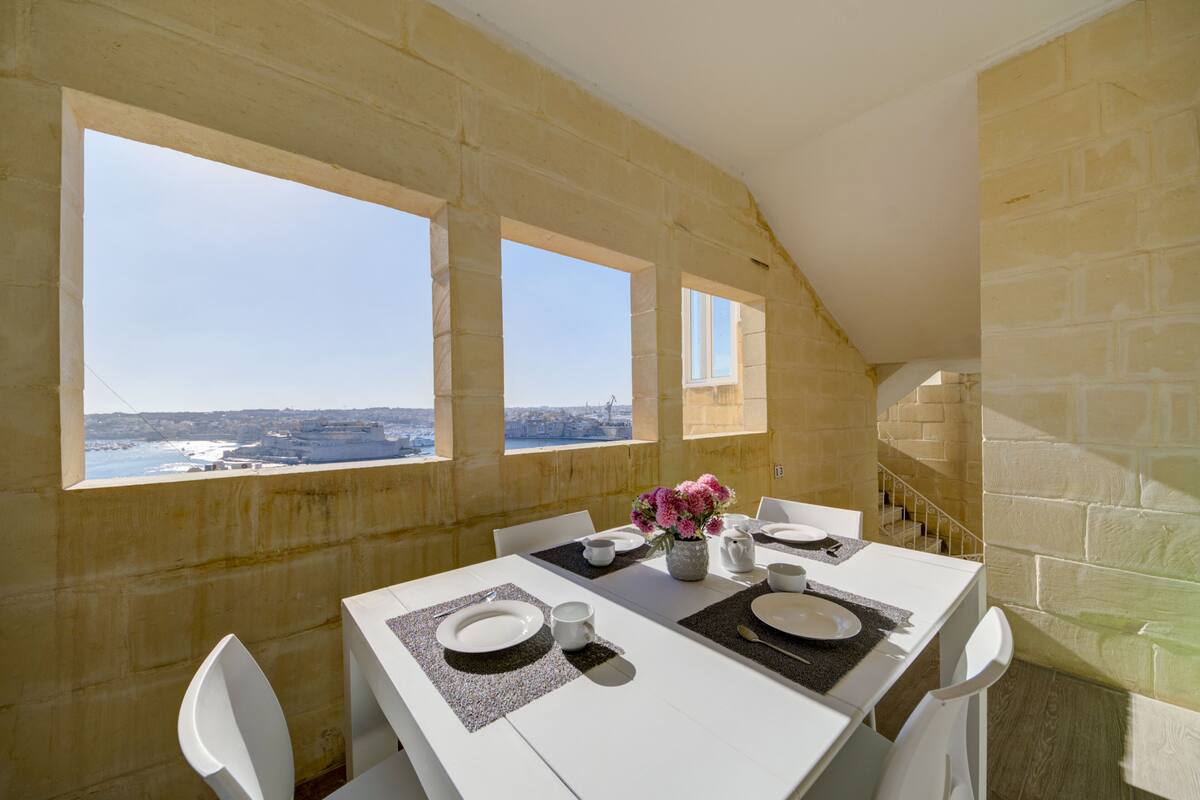 A dining area with a table set for four, large windows, and a view of the sea.