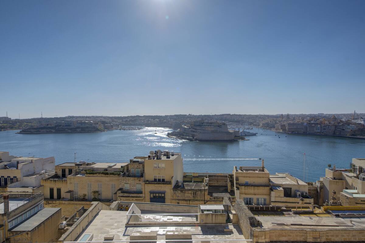 A coastal cityscape with buildings along the waterfront, a clear sky, and a calm sea.