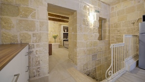 A stone-walled hallway leading to a kitchen area with a white refrigerator and a white bench. - Tritoni harbour suites (Valletta)