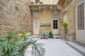Un patio de piedra con una mesa y sillas, plantas en macetas y un cuadro en la pared.