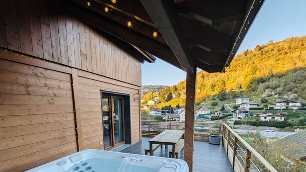 A hot tub on a wooden deck with a view of a village and hills in the background. - Casa de Monzel - Jacuzzi and panoramic view of the Bresse mountains (La Bresse)