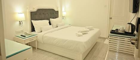 Habitación de hotel con cama, mesitas de noche, escritorio, silla, televisor y cafetera.