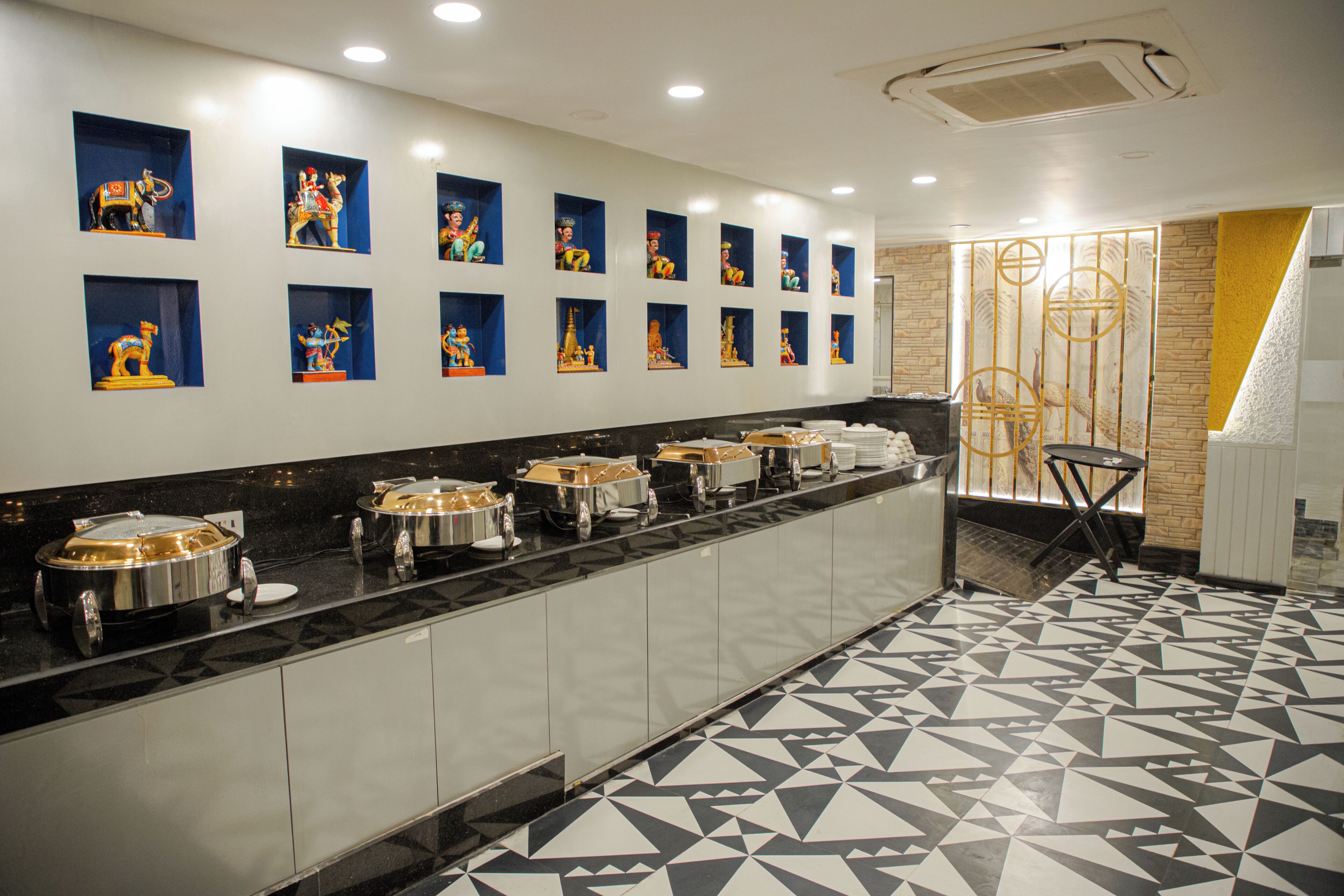 Eine lange Buffetlinie mit mehreren Speiseauslagen, einem gemusterten Boden und einer Wand mit gerahmten Kunstwerken.