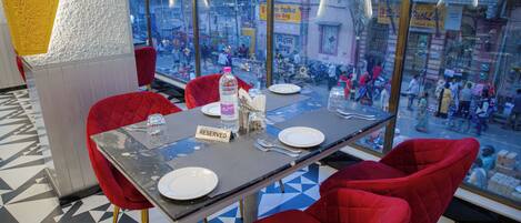 A restaurant with a table set for two, red chairs, and a view of the street through large windows.