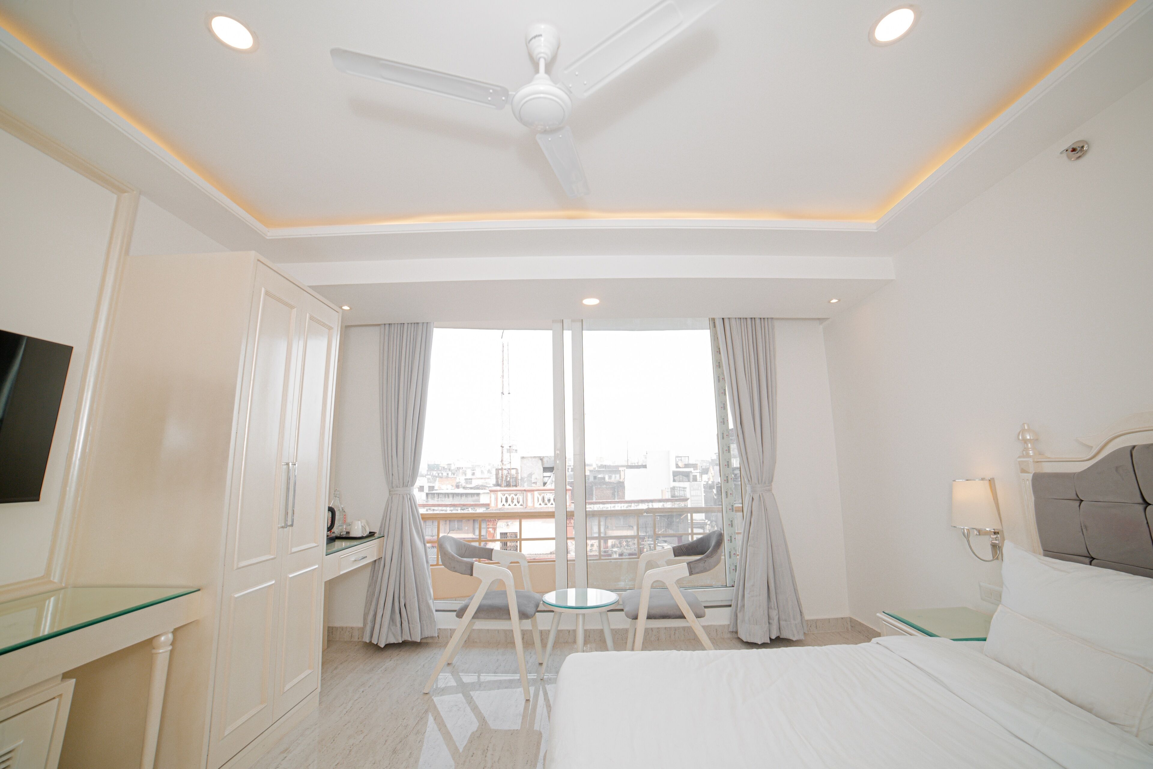 A hotel room with a bed, a desk, a chair, a TV, and a balcony with a view.
