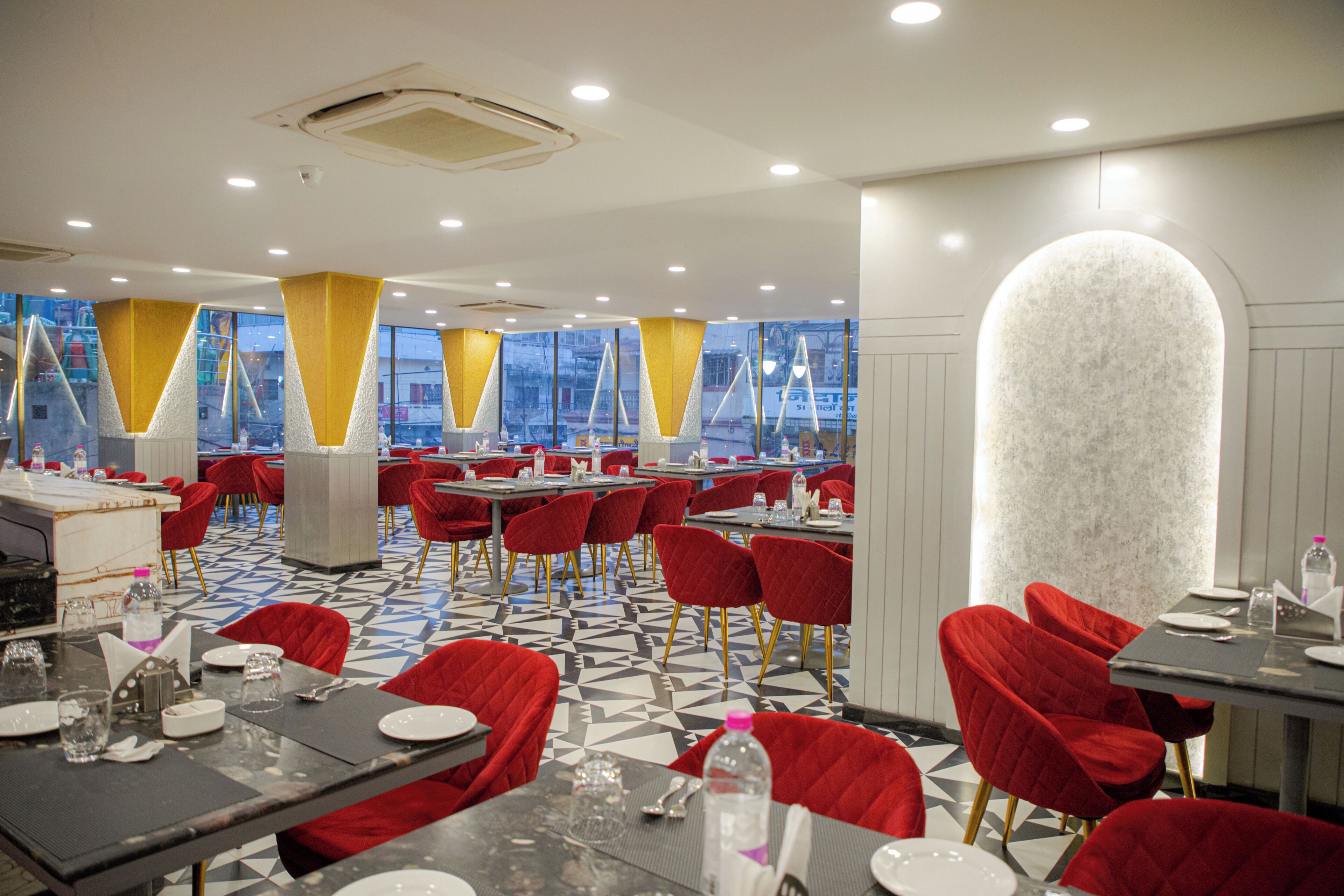 Un espace de restauration moderne avec des chaises rouges, des tables dressées et de grandes fenêtres offrant une vue sur la ville.