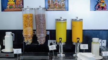 Una barra de desayuno con varios dispensadores de alimentos y bebidas, incluyendo cereales, café, jugo de piña fresca y jugo de mango.