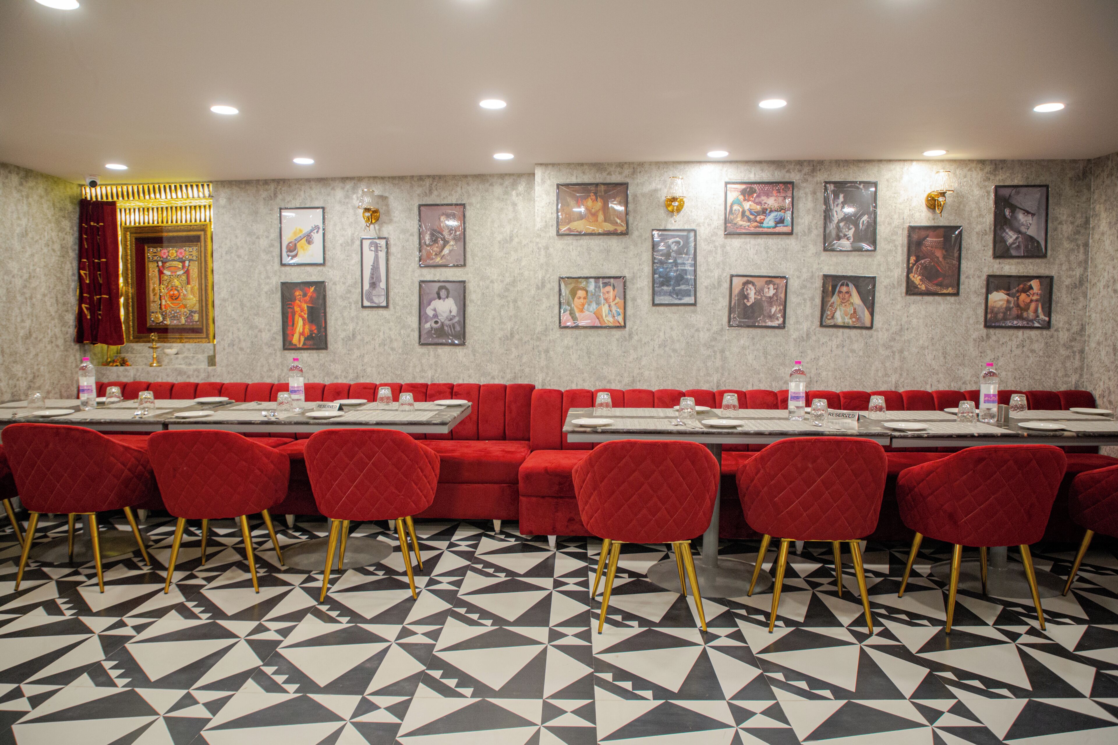Un restaurante con cabinas tapizadas de rojo, piso con estampado blanco y negro, y cuadros en las paredes.