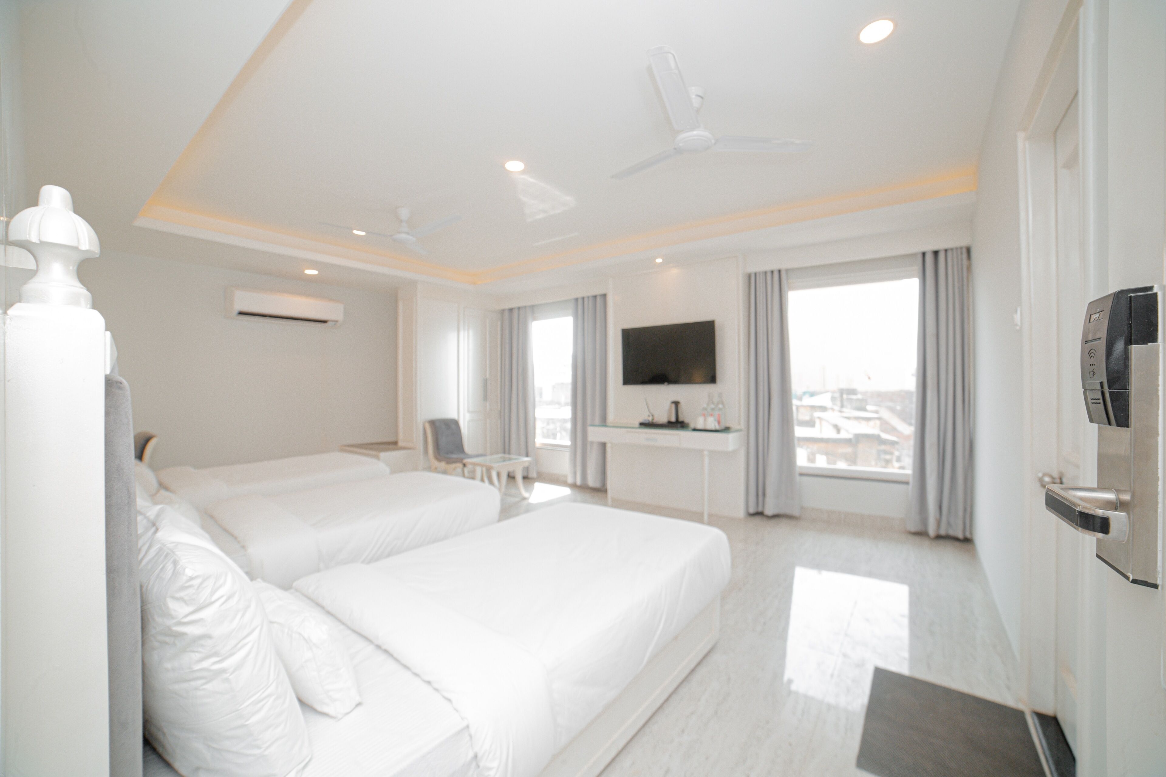 A hotel room with two beds, a desk, a TV, and a view of the city.