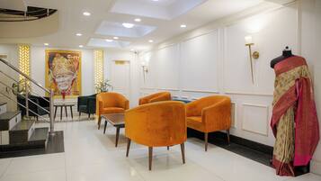 Un hall de hotel con una escalera, sillones naranjas, un maniquí vestido con traje tradicional y un retrato grande en la pared.