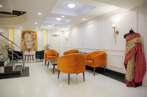 Un hall d’hôtel avec un escalier, des fauteuils orange, un mannequin vêtu d’un costume traditionnel et un grand portrait accroché au mur.
