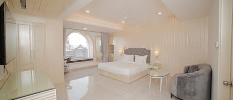 A spacious bedroom with a large bed, a sitting area with a chair, and a glass table.