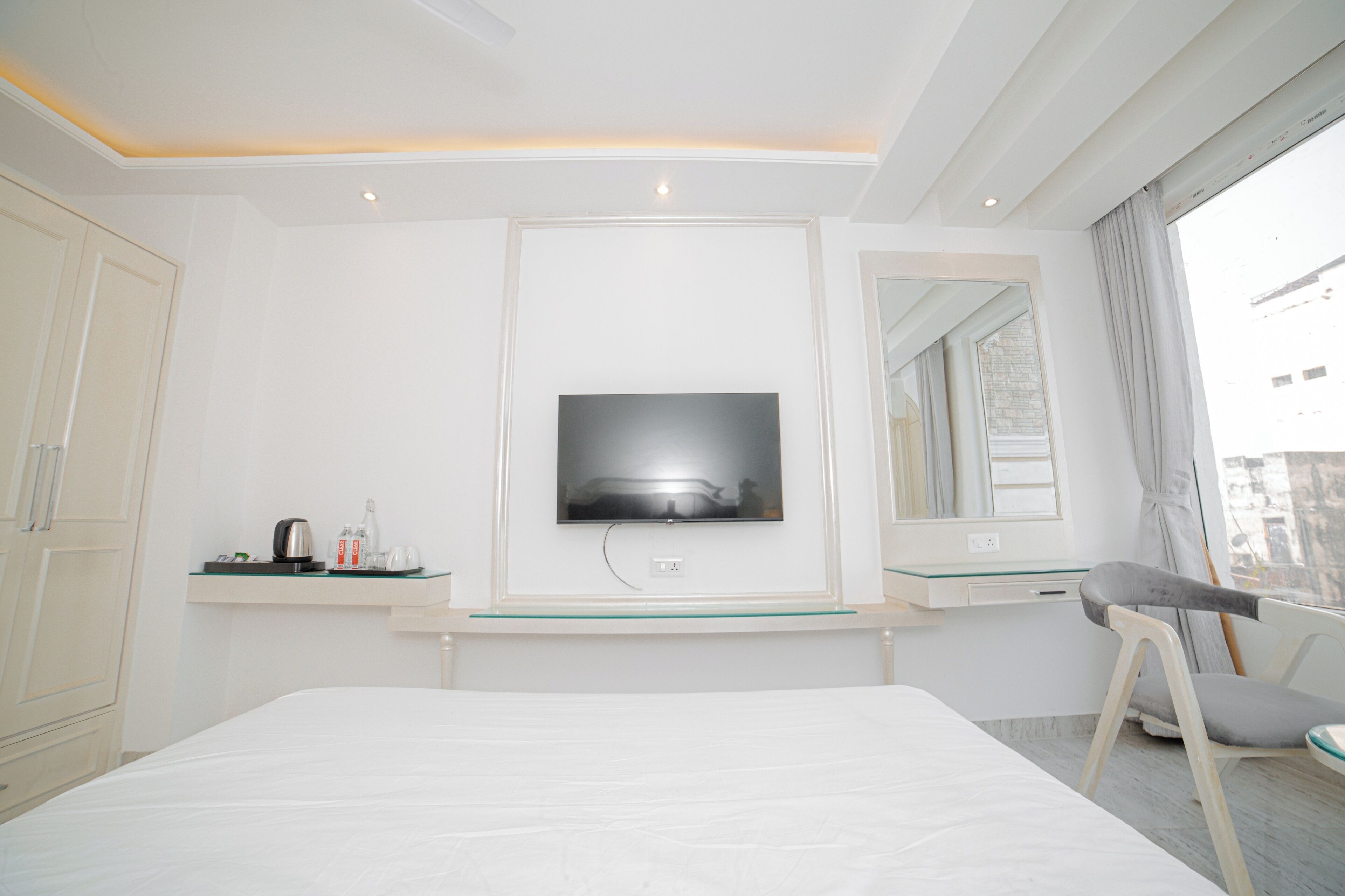 A hotel room with a bed, a TV mounted on the wall, a desk with a chair, and a window with curtains.